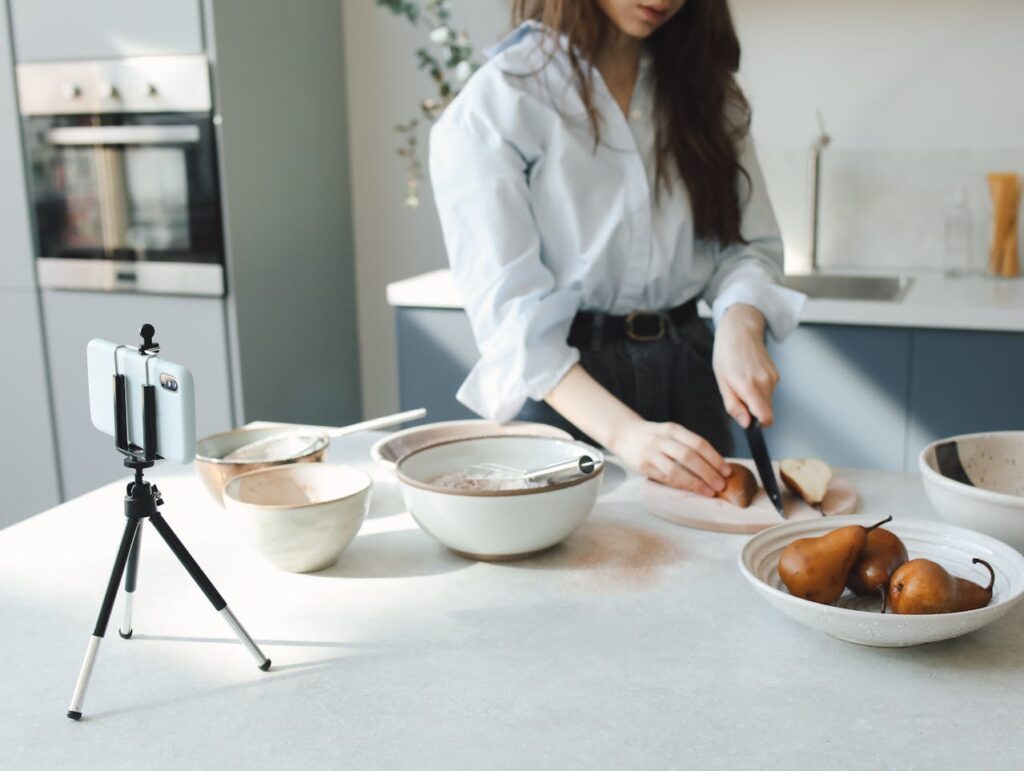A person chopping pears on a cutting board in a kitchen, while a smartphone on a tripod films them.