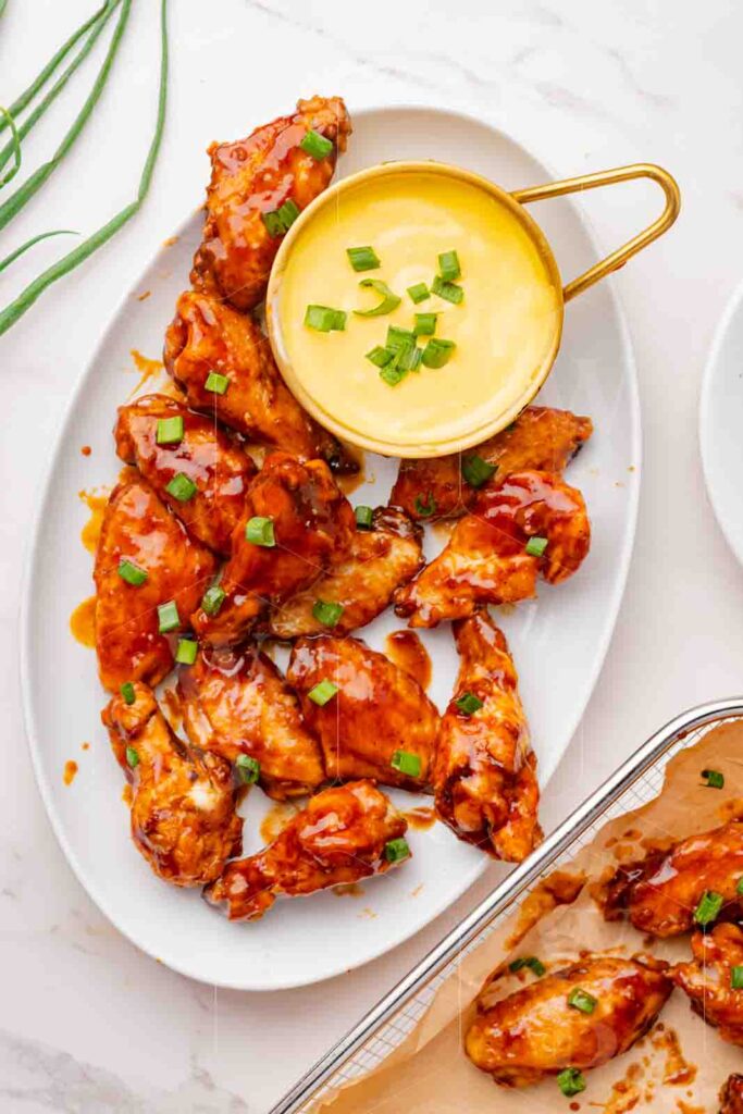 Overhead hero shot of glazed honey BBQ chicken wings on a platter with a dipping sauce