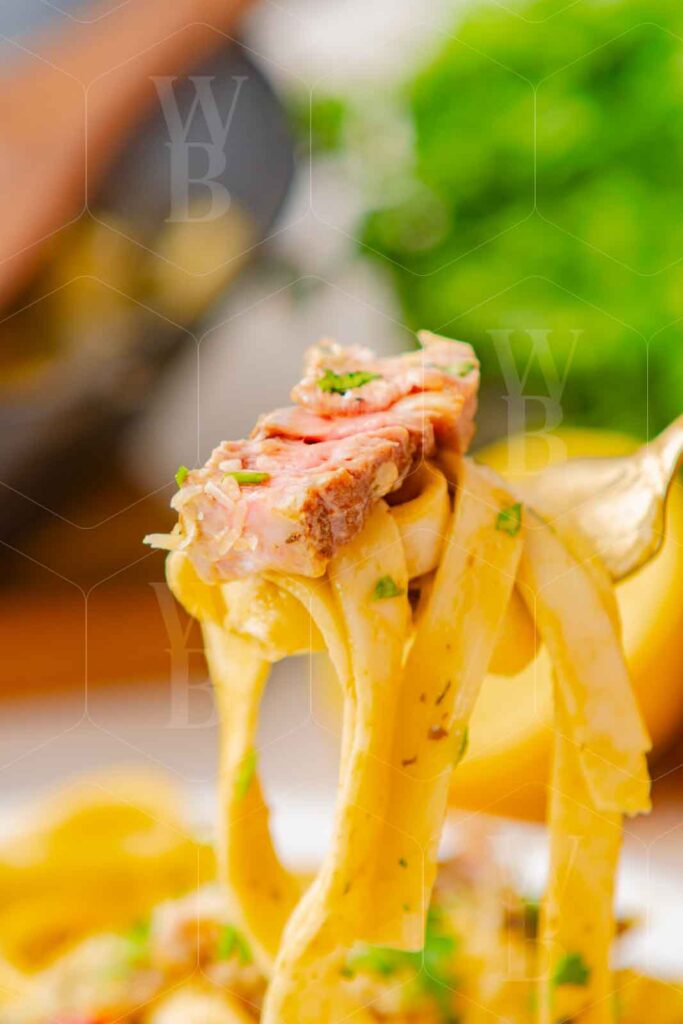 Action shot of a fork lifting fettuccine and a slice of steak from a plate