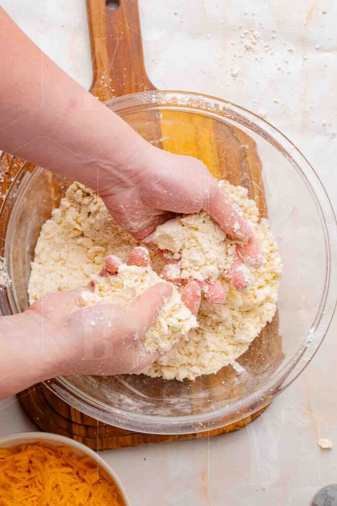 Hands working butter into flour in a glass bowl, a process shot for pumpkin cheddar scones