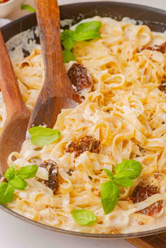 Close-up of creamy fettuccine with fresh basil and wooden spoons in a skillet